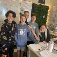 Teacher and 4 of her students standing at her desk with smiles on their faces.